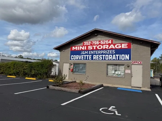 The J&M Storage office, its sign reading 'Mini Storage — J&M Enterprizes — Corvette Restoration' above the phone number 352-796-5264, with marked parking including an accessible bay outside the office door.